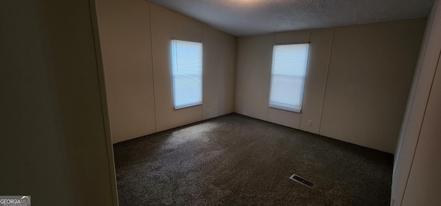 unfurnished room with dark colored carpet, a healthy amount of sunlight, visible vents, and a textured ceiling