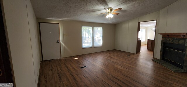 unfurnished living room with a textured ceiling, ceiling fan, dark hardwood / wood-style flooring, and a fireplace