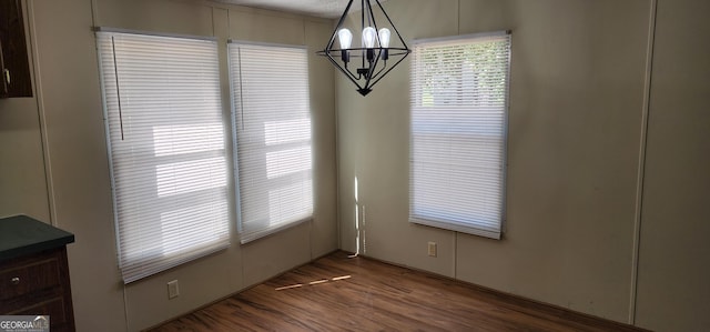 unfurnished dining area featuring dark wood-style flooring and an inviting chandelier