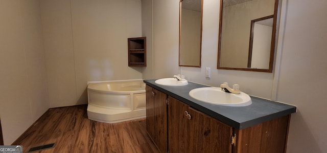 bathroom with double vanity, wood finished floors, a sink, and a bath