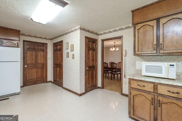 kitchen with a textured ceiling, white appliances, a chandelier, and light tile patterned floors