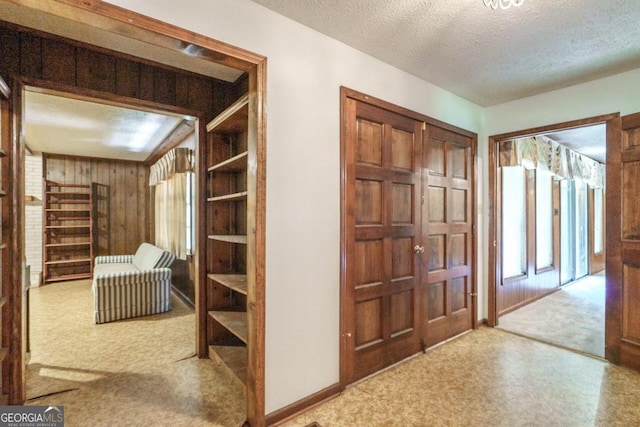 corridor with light carpet, a textured ceiling, and wooden walls