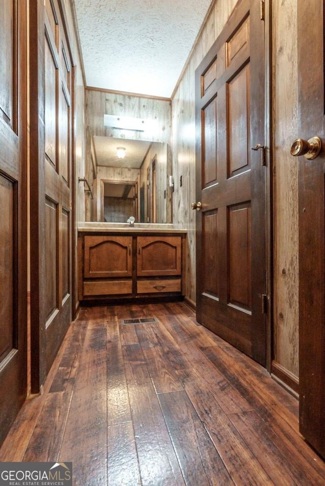 hallway featuring wood walls, dark wood-type flooring, and a textured ceiling