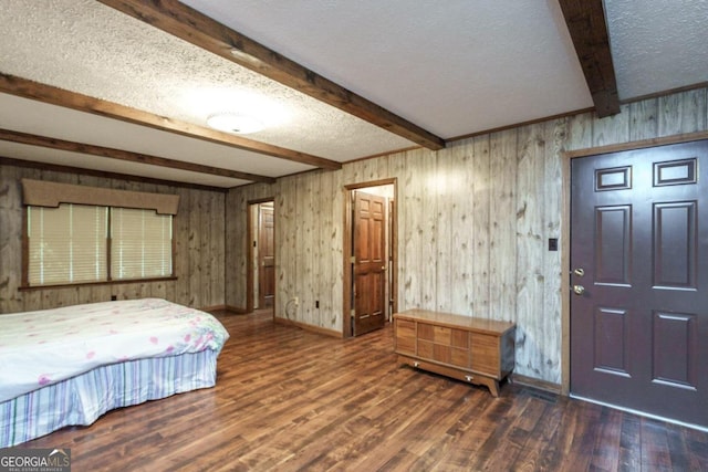 bedroom with a textured ceiling, beam ceiling, wooden walls, and dark hardwood / wood-style floors