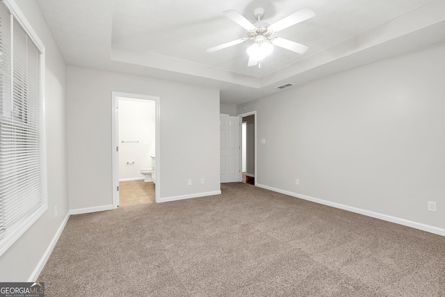 unfurnished bedroom with a tray ceiling, ceiling fan, light carpet, and ensuite bathroom