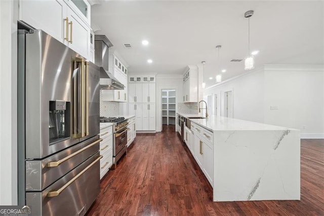 kitchen with dark wood-type flooring, high quality appliances, wall chimney exhaust hood, and tasteful backsplash