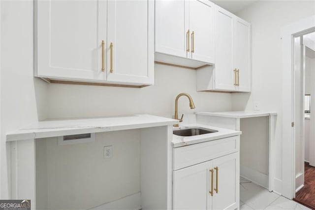 kitchen with sink, light stone counters, white cabinetry, and light wood-type flooring