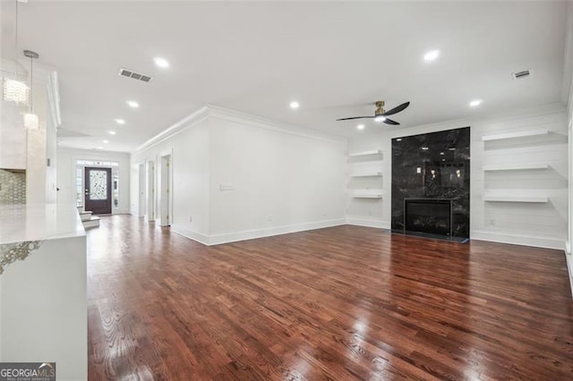 unfurnished living room featuring built in features, dark wood-type flooring, ceiling fan, crown molding, and a high end fireplace