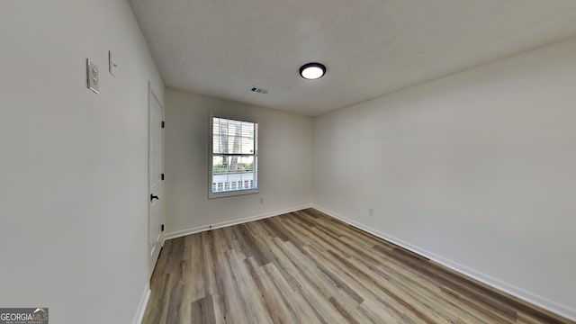 spare room featuring light wood-style floors, visible vents, a textured ceiling, and baseboards