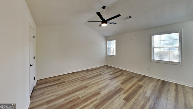 unfurnished room featuring baseboards, visible vents, a ceiling fan, lofted ceiling, and light wood-style floors