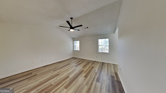 unfurnished room featuring a textured ceiling, light wood-style flooring, visible vents, a ceiling fan, and vaulted ceiling