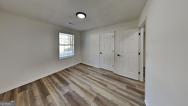 unfurnished bedroom featuring baseboards, visible vents, a textured ceiling, and light wood finished floors