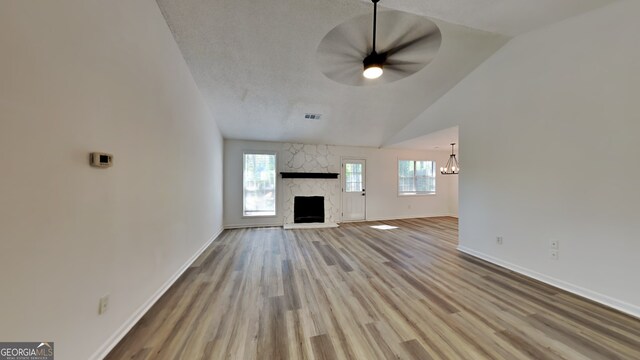 unfurnished living room with hardwood / wood-style floors, ceiling fan with notable chandelier, a stone fireplace, and lofted ceiling