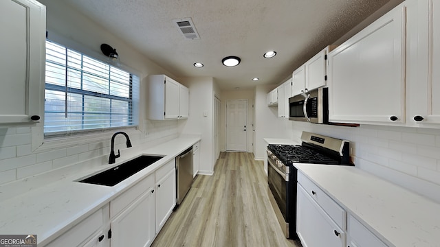 kitchen with stainless steel appliances, a sink, visible vents, white cabinets, and light wood finished floors