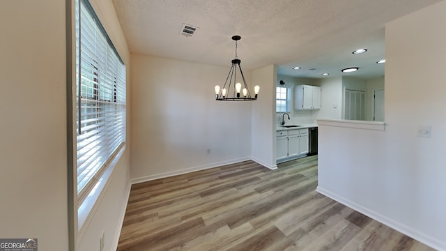 unfurnished dining area featuring visible vents, light wood-style floors, a sink, a textured ceiling, and baseboards