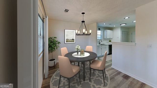 dining area featuring light wood-style floors, visible vents, a notable chandelier, and a textured ceiling