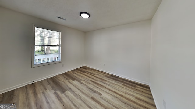 empty room featuring light wood-style floors, baseboards, visible vents, and a textured ceiling