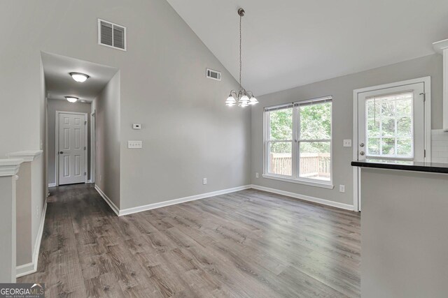 unfurnished dining area with high vaulted ceiling, a chandelier, and wood-type flooring