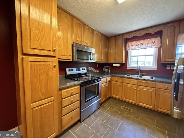 kitchen with stainless steel appliances, brown cabinetry, dark countertops, and a sink