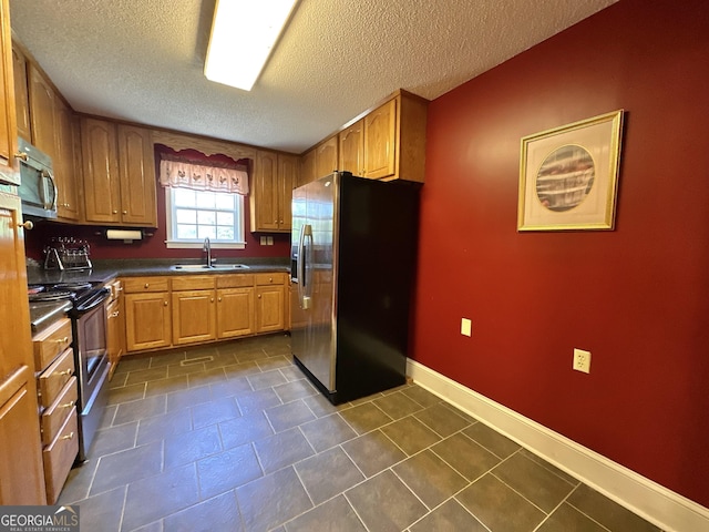 kitchen featuring appliances with stainless steel finishes, dark countertops, brown cabinets, and a sink