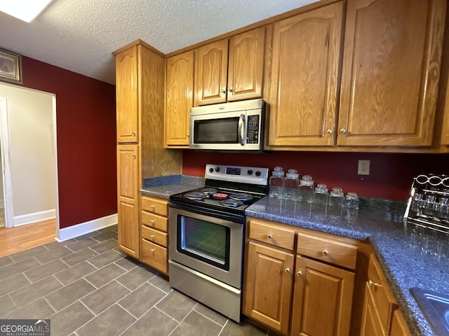 kitchen with brown cabinetry, baseboards, stainless steel appliances, and a textured ceiling