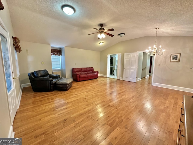 living room featuring baseboards, vaulted ceiling, a textured ceiling, light wood-style floors, and ceiling fan with notable chandelier