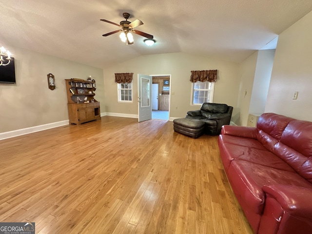 living area with light wood finished floors, vaulted ceiling, ceiling fan, a textured ceiling, and baseboards