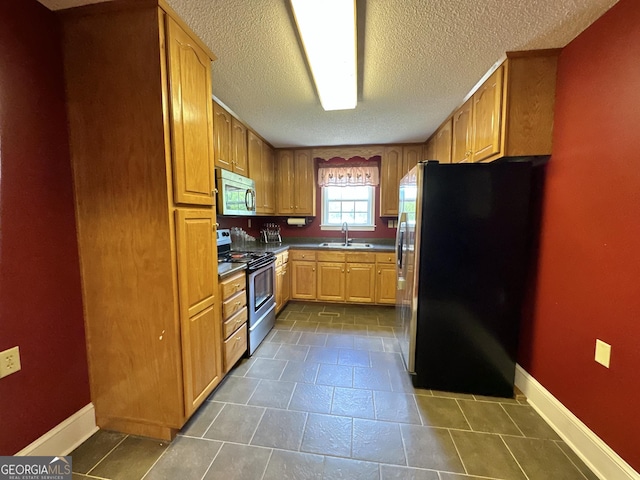 kitchen featuring a textured ceiling, stainless steel appliances, a sink, baseboards, and dark countertops