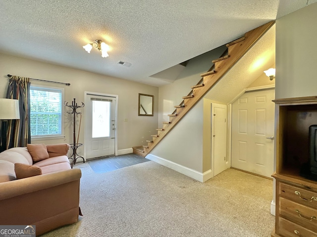 living room featuring a textured ceiling, carpet floors, visible vents, baseboards, and stairs