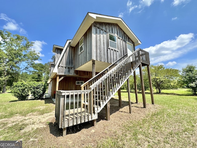 exterior space featuring board and batten siding, a lawn, a wooden deck, and stairs