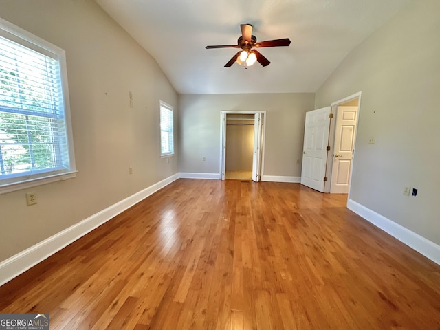 unfurnished bedroom with lofted ceiling, light wood-style flooring, a ceiling fan, baseboards, and a closet