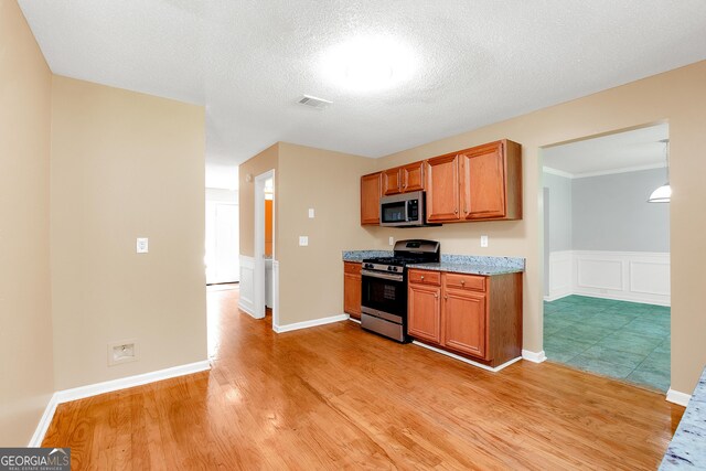 kitchen with light wood-type flooring, a textured ceiling, appliances with stainless steel finishes, and light stone counters