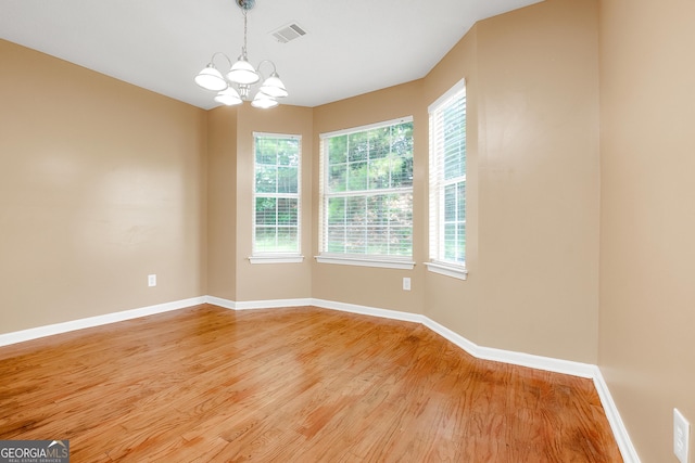 empty room with an inviting chandelier, visible vents, baseboards, and wood finished floors