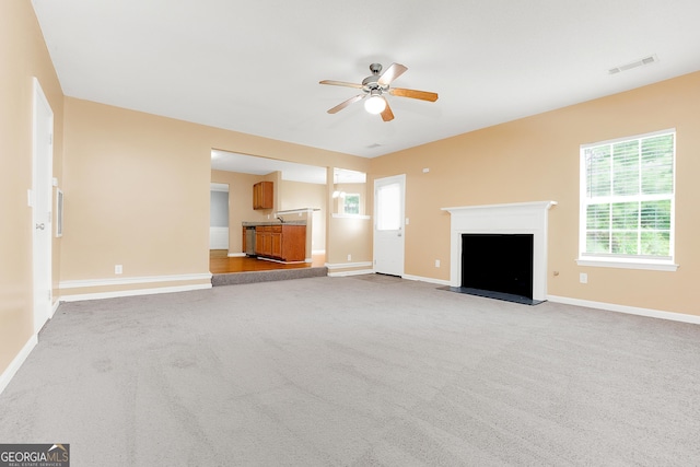 unfurnished living room with ceiling fan, light colored carpet, a fireplace, visible vents, and baseboards