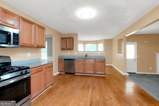 kitchen featuring light wood-style flooring, appliances with stainless steel finishes, brown cabinets, light stone countertops, and a sink