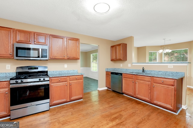 kitchen with stainless steel appliances, a chandelier, sink, light stone counters, and light wood-type flooring