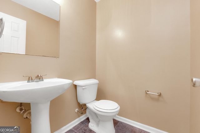 half bath featuring toilet, tile patterned flooring, baseboards, and a sink