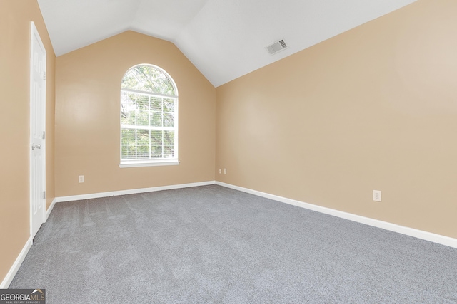 empty room with lofted ceiling, carpet floors, baseboards, and visible vents