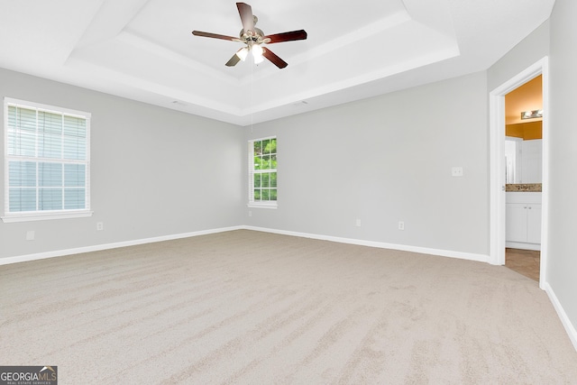 unfurnished room with ceiling fan, a raised ceiling, light colored carpet, and baseboards