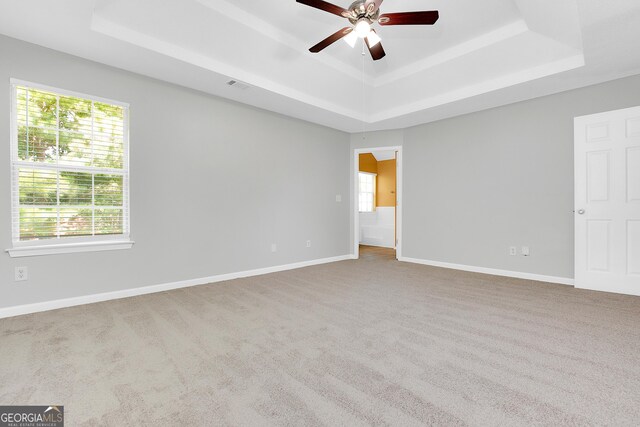 empty room with ceiling fan, carpet floors, and a tray ceiling