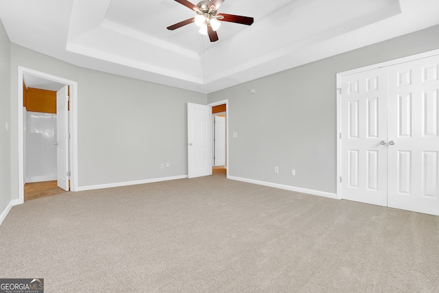 unfurnished bedroom featuring ceiling fan, a closet, carpet floors, and a tray ceiling