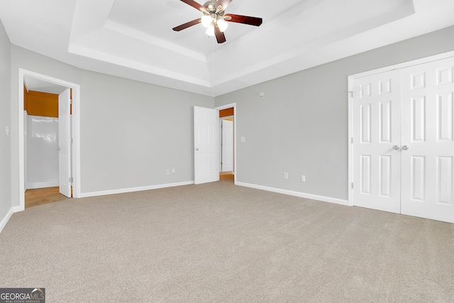 unfurnished bedroom featuring baseboards, ceiling fan, a raised ceiling, and light colored carpet