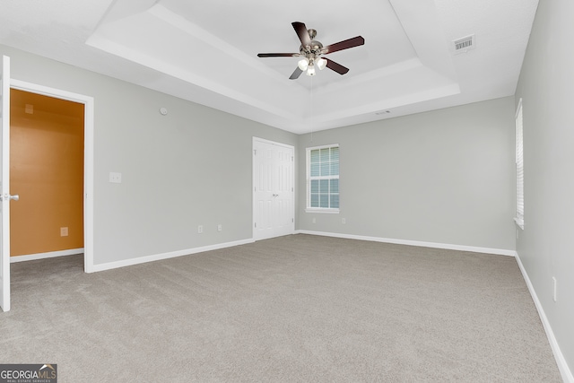 carpeted spare room with ceiling fan and a raised ceiling