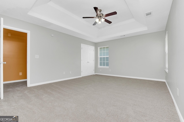 unfurnished room featuring a ceiling fan, visible vents, a tray ceiling, and baseboards