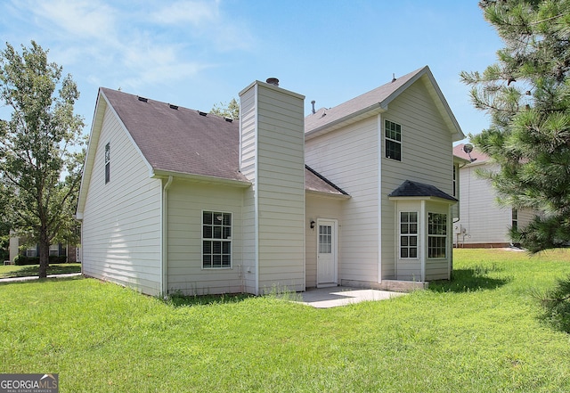 rear view of property with a shingled roof, a chimney, and a lawn