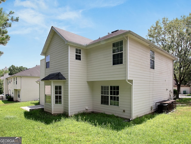 rear view of house with central AC unit and a lawn