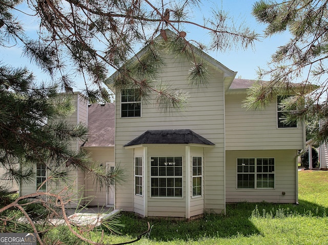 back of house featuring a shingled roof, a chimney, and a lawn