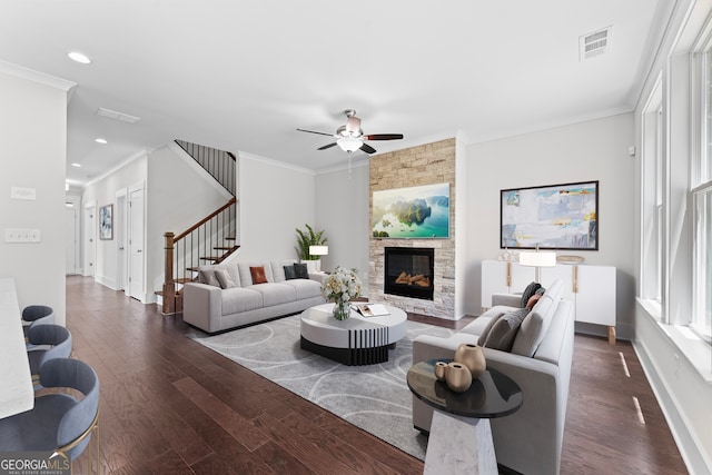 living room featuring ceiling fan, dark hardwood / wood-style floors, crown molding, and a stone fireplace