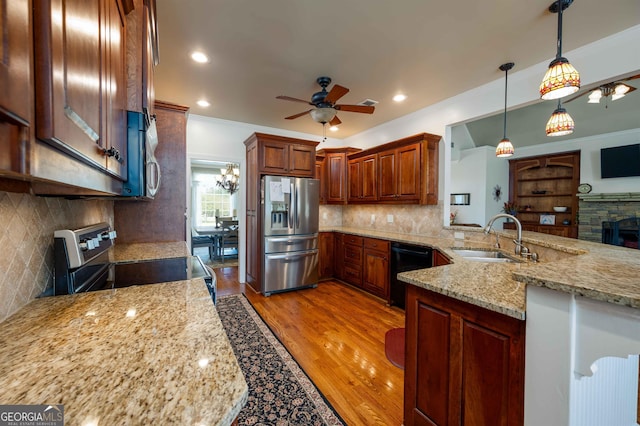 kitchen featuring light wood-type flooring, ceiling fan with notable chandelier, appliances with stainless steel finishes, sink, and a fireplace