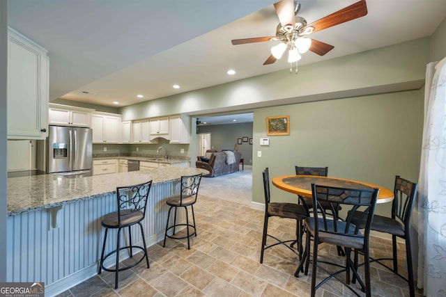 kitchen featuring stainless steel appliances, sink, a kitchen breakfast bar, ceiling fan, and light tile patterned flooring